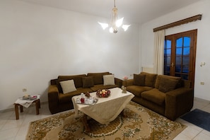 A living room with two brown sofas, a small table with a white tablecloth, a chandelier, and a view of the outdoors through a window.