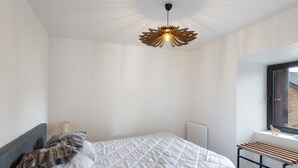 Un dormitorio con cama, ventana, radiador y una lámpara de techo original.