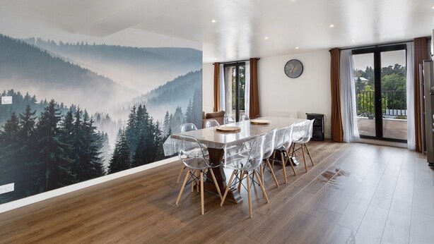 Comedor con mesa y sillas, un mural de una montaña boscosa y vistas a través de un ventanal.