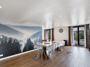 A dining area with a table and chairs, a mural of a forested mountain, and a view through a glass door. - Comfortable Mountain Stay in Formiguères: 4 Bedrooms, 9 min to Slopes, Private Terrace! (Formiguères)