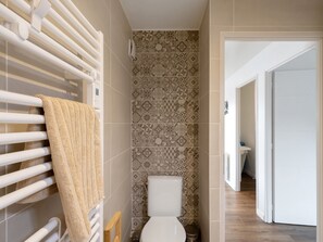 Ein Badezimmer mit Toilette, gemusterten Fliesen, einem Handtuchhalter und einem hölzernen Rahmen.