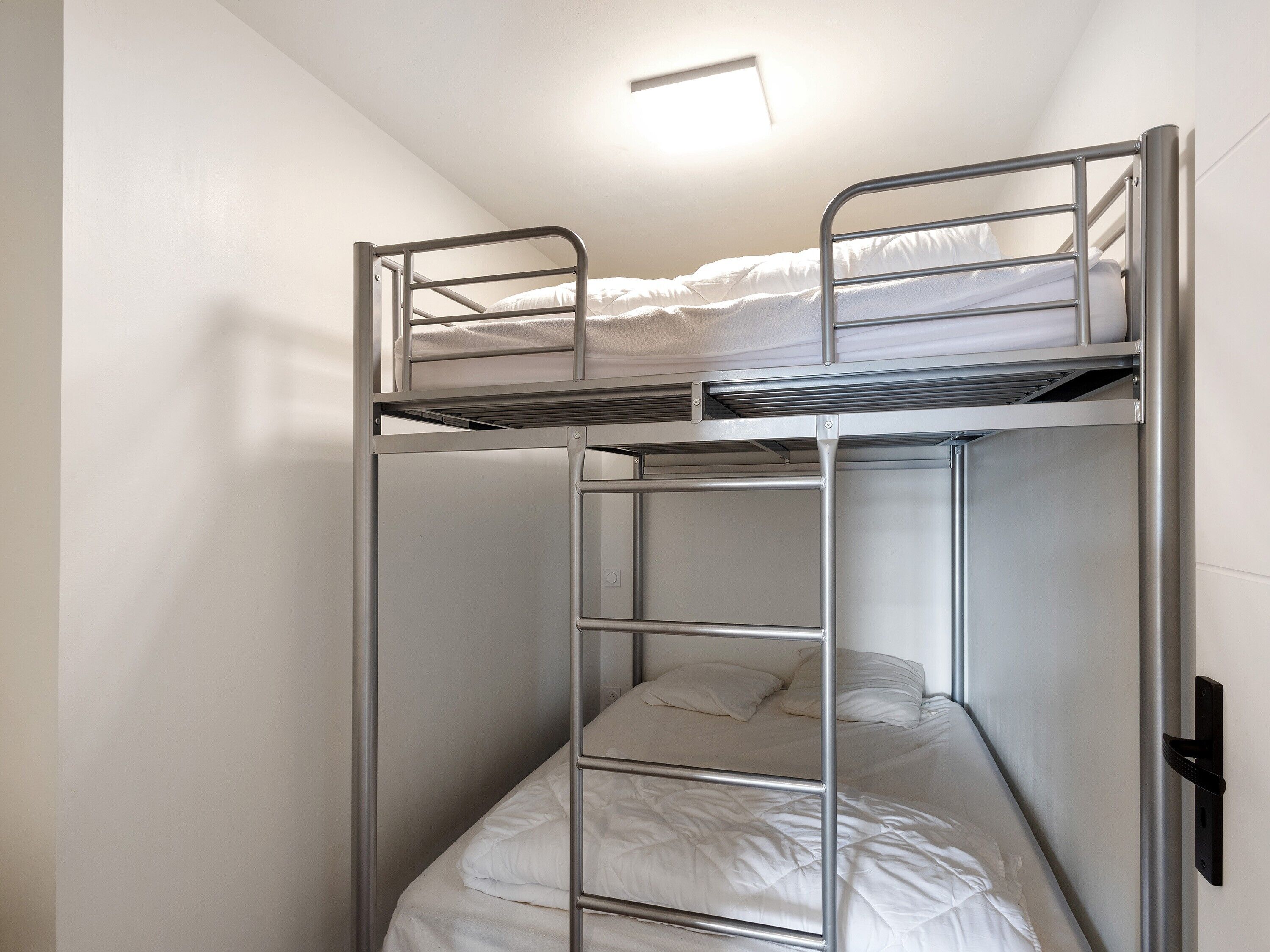 Ein Stockbett mit einer Leiter, ein Einzelbett darunter und eine Leuchte darüber.