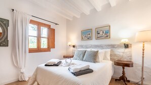 Una cama bien hecha con cabecera, dos lámparas de noche y una ventana con cortinas.