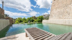 Una piscina con cubierta de madera, rodeada de muros de piedra y follaje.