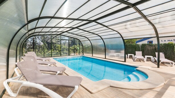 Une piscine couverte dotée de chaises longues et d’une structure en verre.