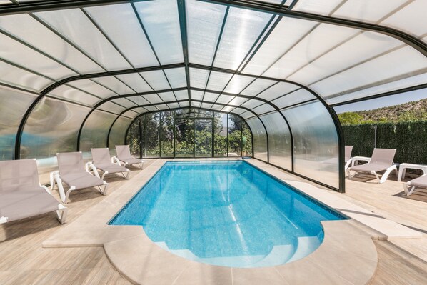 A swimming pool with a glass enclosure, surrounded by lounge chairs.