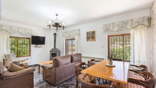 A living room with a sofa, a dining table, chairs, a TV, a fireplace, and large windows. - Apartment 'Villacalar Il' with Mountain View, Private Garden and Wi-Fi (Calar de la Santa)