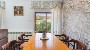 A conference room with a long wooden table, six wooden chairs, a decorative vase, a stone wall, a window with a view, and a patterned wall hanging. - Apartment 'Villacalar Il' with Mountain View, Private Garden and Wi-Fi (Calar de la Santa)
