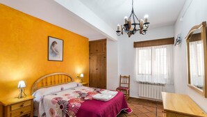 A bedroom with a bed, nightstands, a wooden wardrobe, a chair, a wooden desk, a chandelier, and a window with curtains. - Apartment 'Villacalar Ill' with Mountain View, Private Terrace and Wi-Fi (Calar de la Santa)