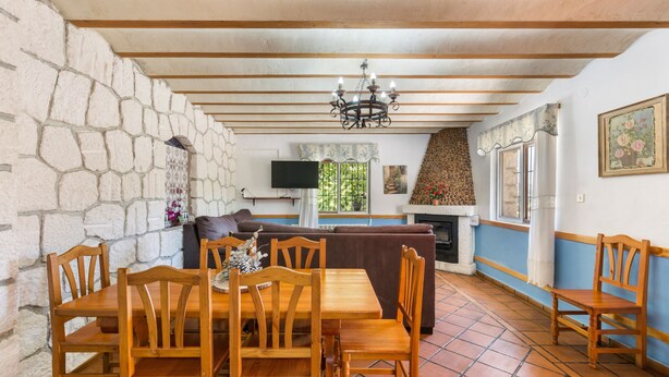A dining area with a stone wall, wooden furniture, a chandelier, and a television. - Apartment 'Villacalar Ill' with Mountain View, Private Terrace and Wi-Fi (Calar de la Santa)