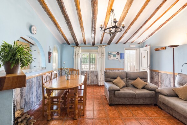 Uma área de refeições com mesa e cadeiras de madeira, um sofá cinzento e um vaso com planta.