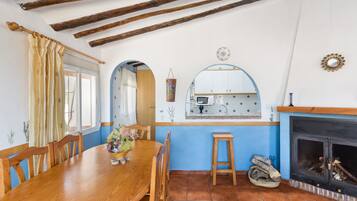 Un coin repas avec une table et des chaises en bois, une cuisine équipée d’une cuisinière et une cheminée.