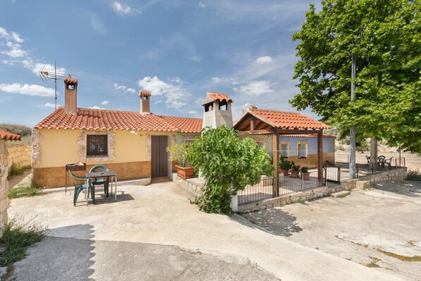 A two-story building with a tiled roof, a balcony, and a small patio area with a table and chairs.