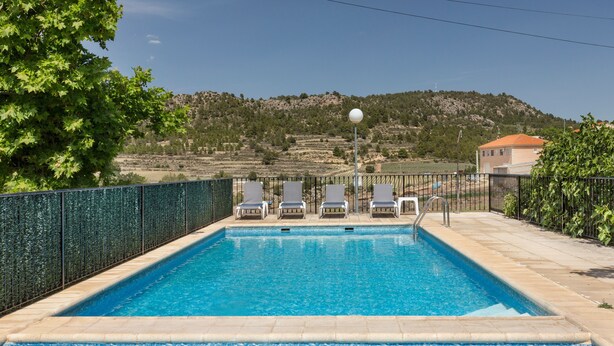 Una piscina rectangular con agua cristalina azul, rodeada por una valla baja y sillas de descanso.