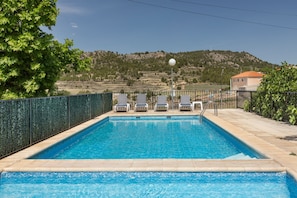 A rectangular swimming pool with clear blue water, surrounded by a low fence and lounge chairs.
