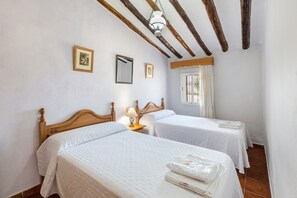 A hotel room with two beds, wooden beams on the ceiling, a window with curtains, and a wall-mounted mirror.