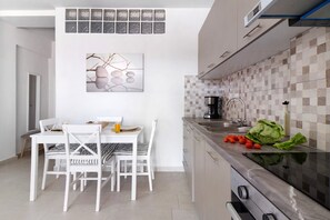 Una cocina moderna con salpicadero de azulejos, una zona de comedor con mobiliario blanco y una obra de arte colgada en la pared.