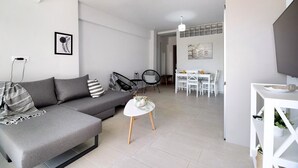 Uma sala de estar moderna com um sofá cinza, uma mesa pequena branca e um aparador de TV.