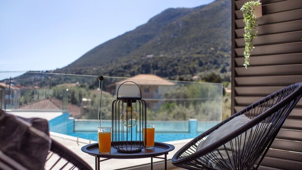Varanda com mesa, duas cadeiras, planta pendente e vista para a montanha e piscina.
