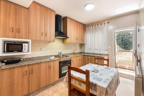 A kitchen with wooden cabinets, a microwave, a stove, and a dining table with chairs. - Apartment 'Duplex Rural' with Mountain View, Private Terrace and Wi-Fi (Calar de la Santa)