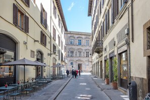 Uma rua estreita com mesas ao ar livre, um edifício com porta azul e céu claro.