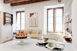 Un comedor con una mesa blanca, un pastel con fruta, una silla blanca y una ventana con cortinas.