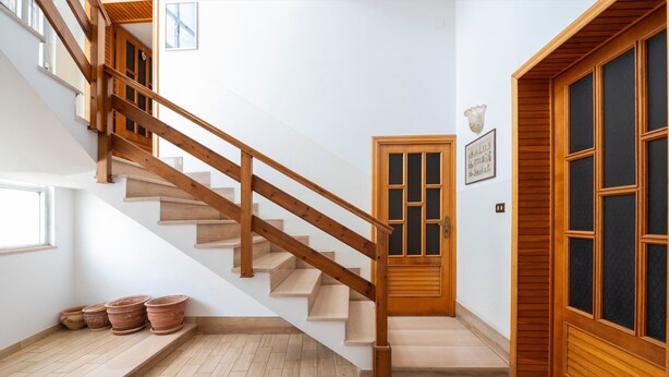 A wooden staircase with a handrail, a door with glass panels, and a wall-mounted light fixture.