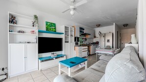 Una sala de estar moderna con un televisor de pantalla plana, ventilador de techo, sofá y una zona de cocina.