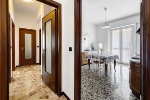 A hallway with stone flooring, wooden doors, and a dining area with a table and chairs.