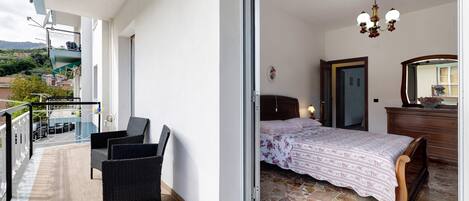 Ein Balkon mit Korbstühlen, ein Bett mit Blumenmuster-Bettwäsche, ein Schminktisch und eine Chandelier.