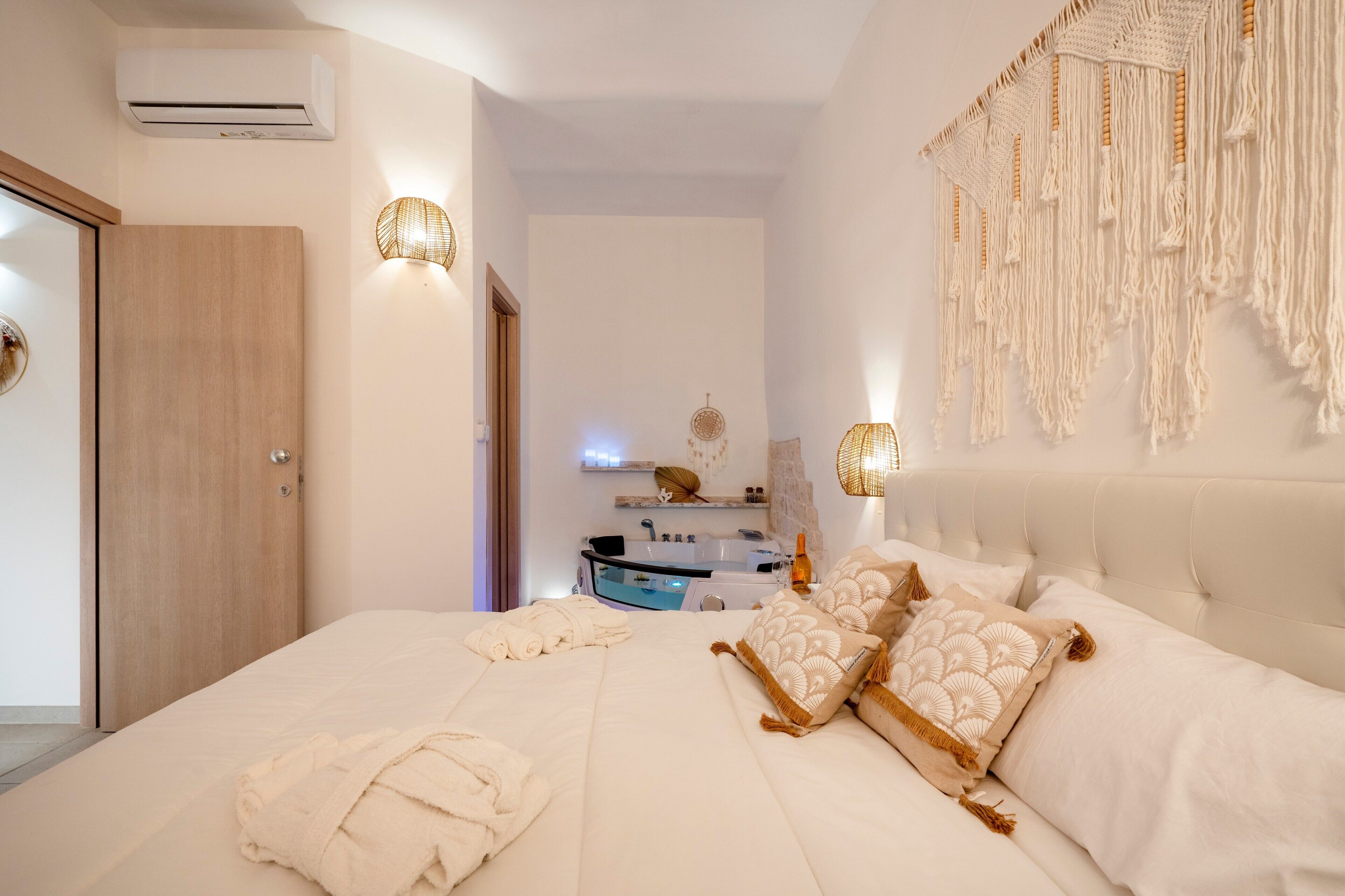 A bedroom with a bed, bedside lamps, a wall-mounted macrame piece, a vanity with a mirror, and an air conditioning unit.