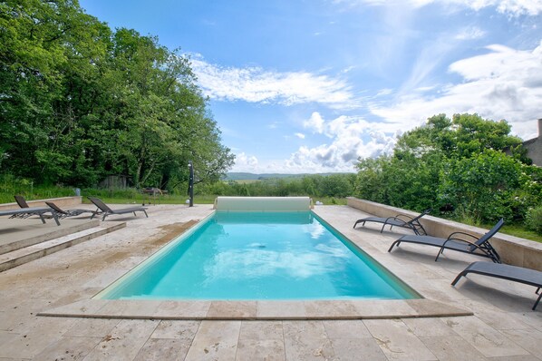 A rectangular swimming pool with a clear blue water surface, surrounded by a stone deck.