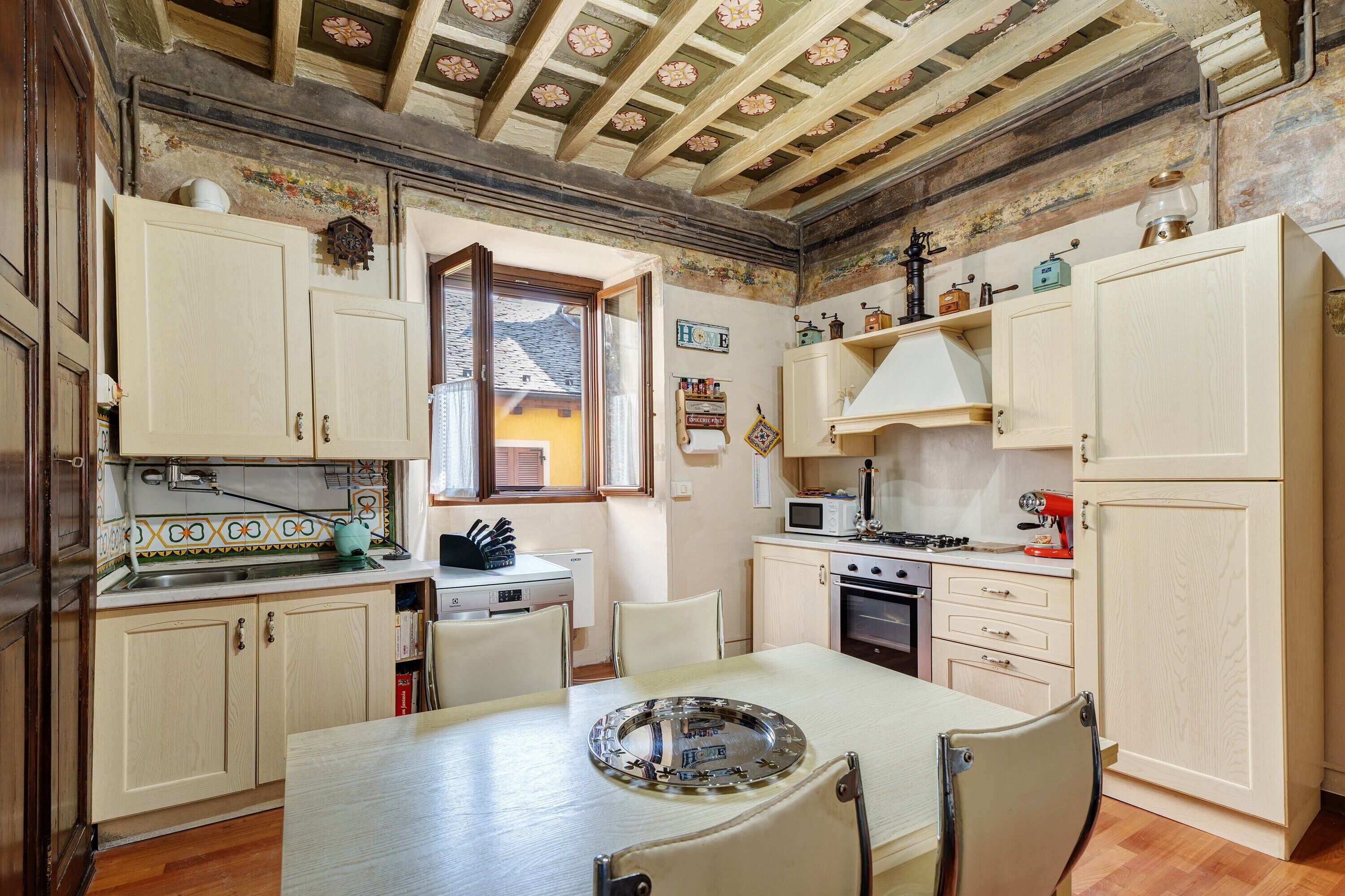 Une cuisine avec des meubles de rangement en bois, une table à manger, des chaises, une fenêtre et un four à micro-ondes.