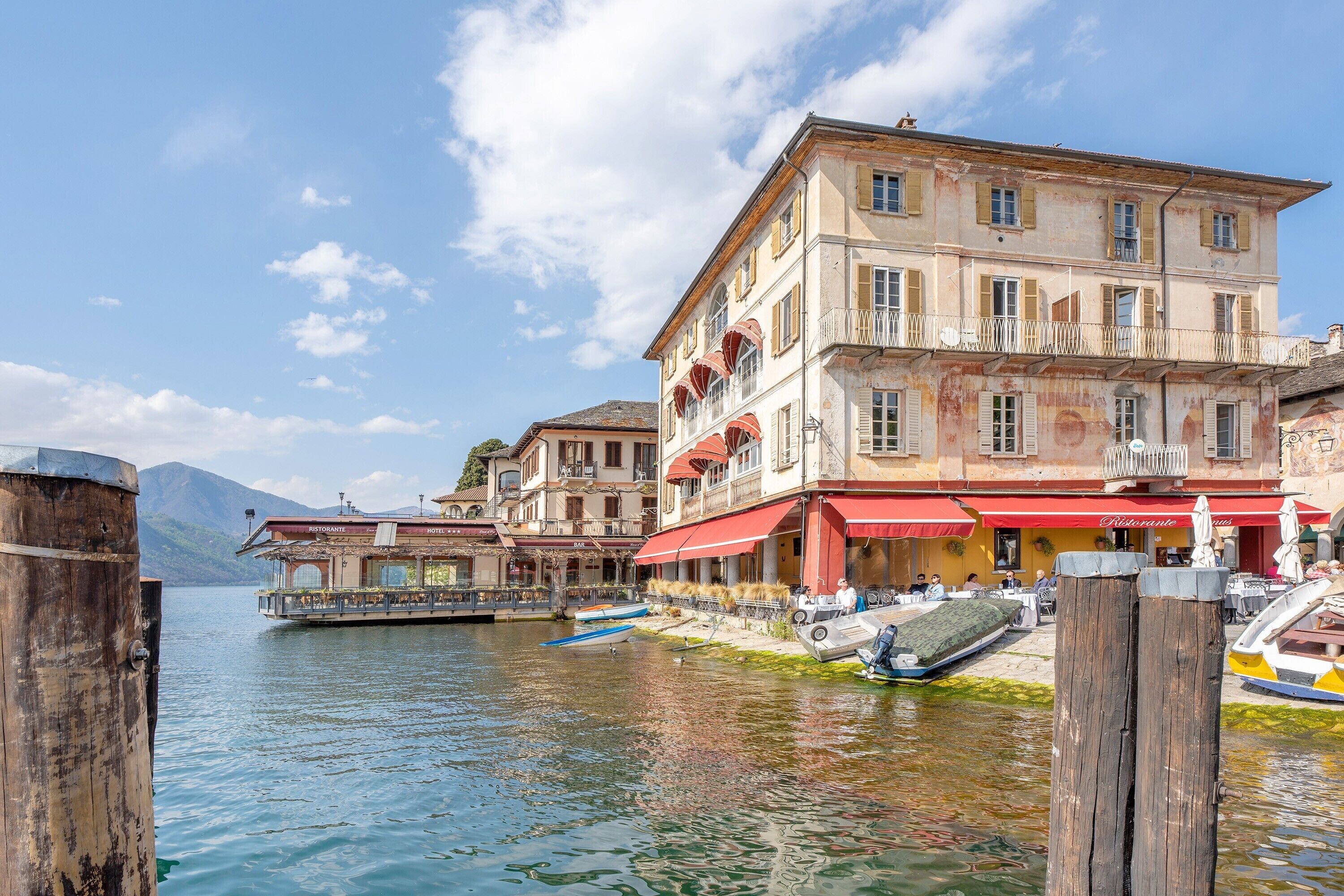 A waterfront building with balconies, a restaurant with red awnings, and boats docked nearby.