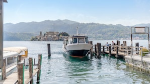A boat docked at a pier with a mountainous backdrop. - Apartment 'Antro Di Circe - Orta Centro' with Private Terrace, Garden and Wi-Fi (Orta San Giulio)