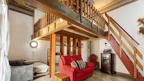 A room with a red sofa, a grey sofa, a wooden cabinet, and a staircase with wooden railings. - Apartment 'Antro Di Circe - Orta Centro' with Private Terrace, Garden and Wi-Fi (Orta San Giulio)