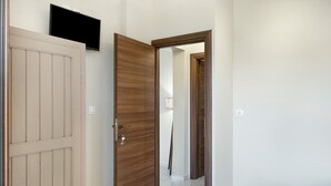 A hallway with a wooden door, a television mounted on the wall, and a bed with a blue blanket. - Apartment 'Akrogiali House Drimonas' with Sea View, Wi-Fi and Air Conditioning (Leros)