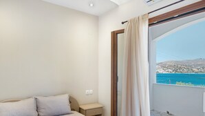 A bedroom with a bed, a nightstand, a window with curtains, and a view of a coastal landscape. - Apartment 'Akrogiali House Drimonas' with Sea View, Wi-Fi and Air Conditioning (Leros)