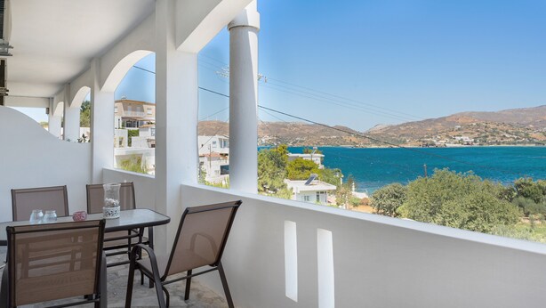 A balcony with a table and chairs, overlooking a coastal landscape with buildings and hills. - Apartment 'Akrogiali House Drimonas' with Sea View, Wi-Fi and Air Conditioning (Leros)