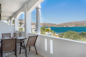 Un balcon avec une table et des chaises, donnant sur un paysage côtier avec des bâtiments et des collines.