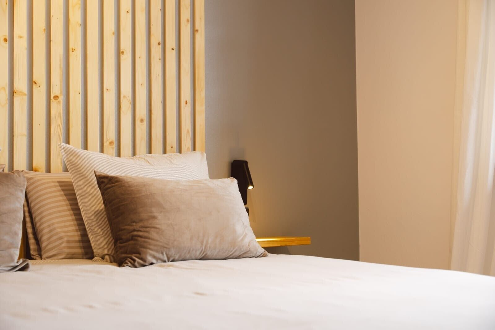 Una cama con varias almohadas, un cabecero de madera, una mesita de noche con una lámpara y una pared lisa.