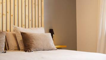 Una cama con varias almohadas, un cabecero de madera, una mesita de noche con una lámpara y una pared lisa.