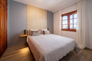 Une chambre avec un grand lit, un mur recouvert de lambris en bois, une fenêtre avec des rideaux et un plancher en bois.