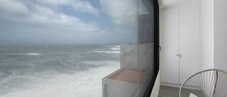 A balcony with a view of the ocean, a wicker chair, and a white wardrobe.
