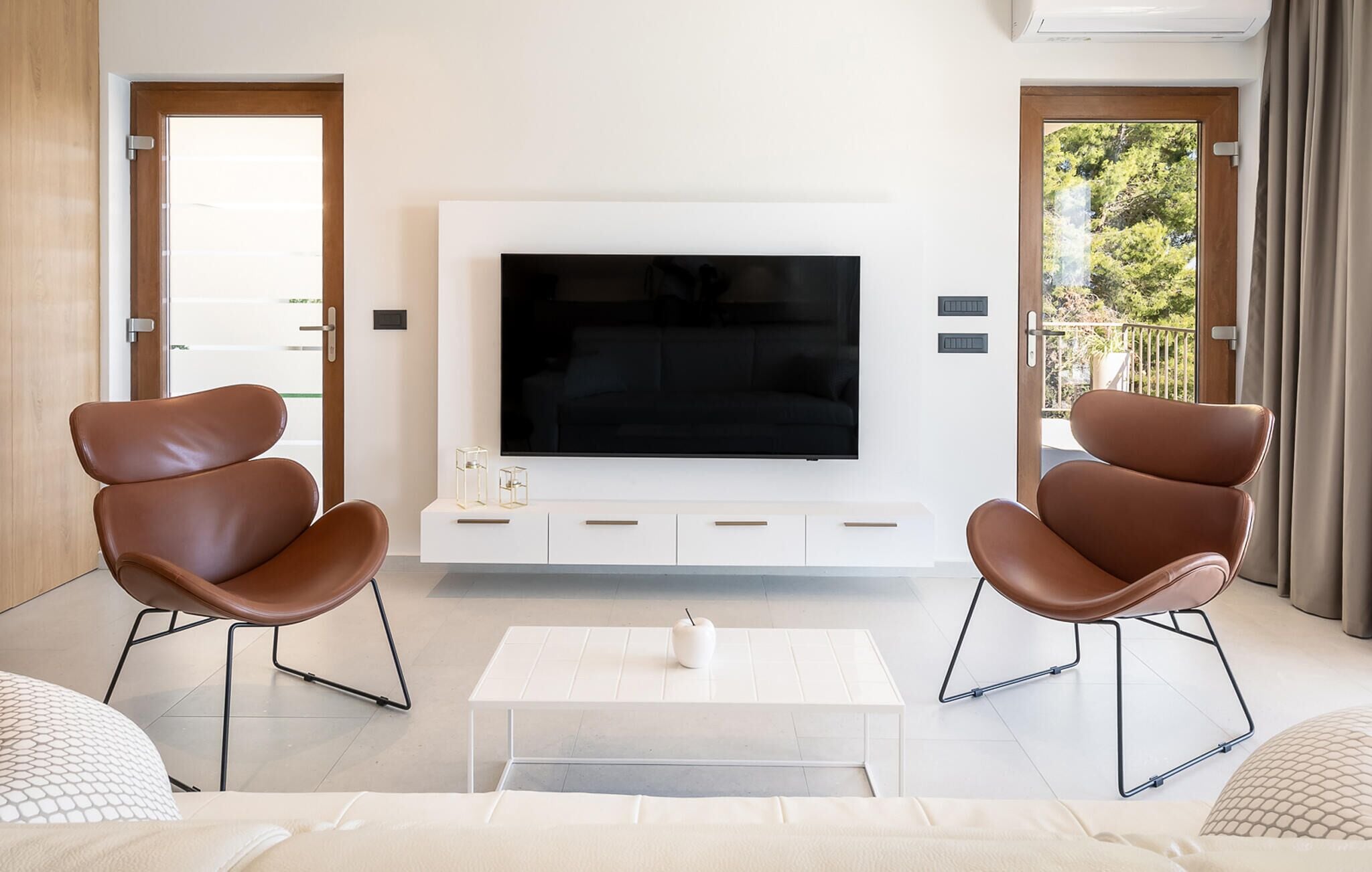 Ein modernes Wohnzimmer mit einem großen Flachbildfernseher, zwei Ledersesseln, einem weißen Couchtisch und einer Couch.