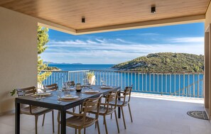 Un coin repas avec une table dressée pour quatre personnes, offrant une vue panoramique sur la côte, avec une terrasse en bois et une rambarde.