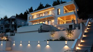 Una casa moderna de varios pisos con balcones, una escalera e iluminación exterior.