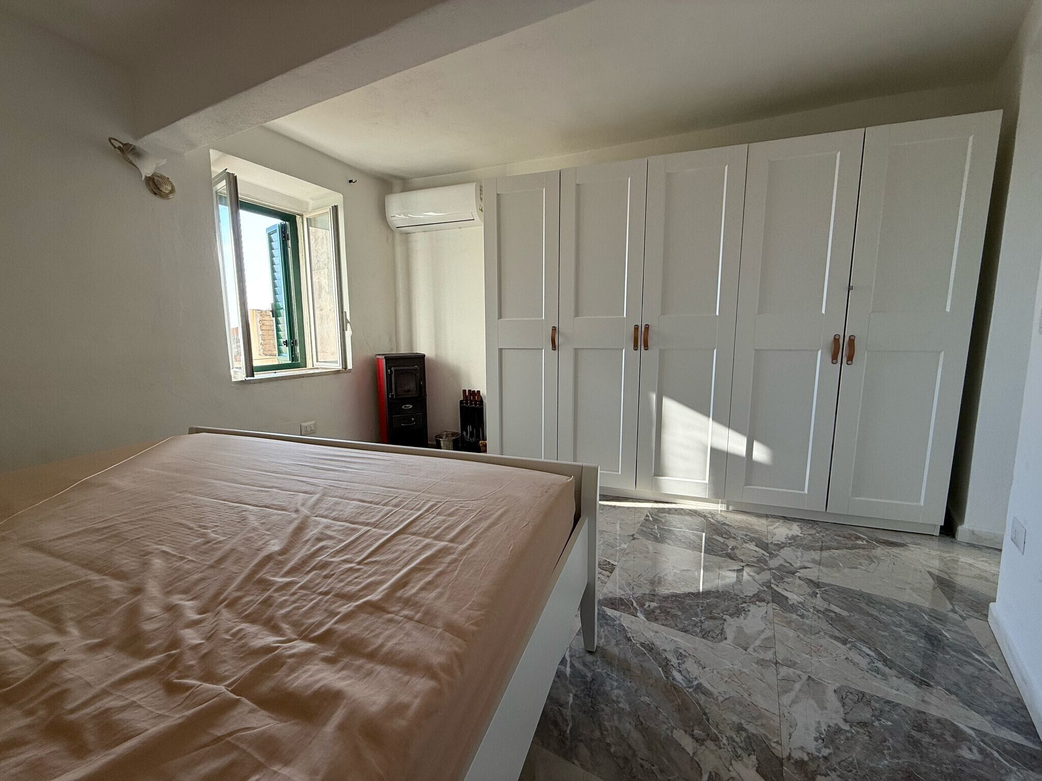 Een slaapkamer met een bed, een raam, een kledingkast en een verwarming.