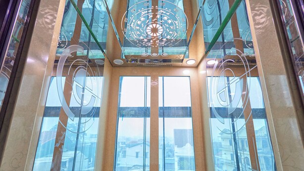Un interior moderno con un hueco para ascensor de vidrio, una lámpara decorativa central y vistas de edificios.