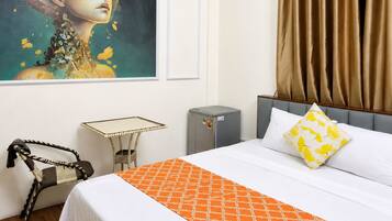 A hotel room with a large painting on the wall, a bed with an orange bedspread, a grey headboard, and a grey bedside table.